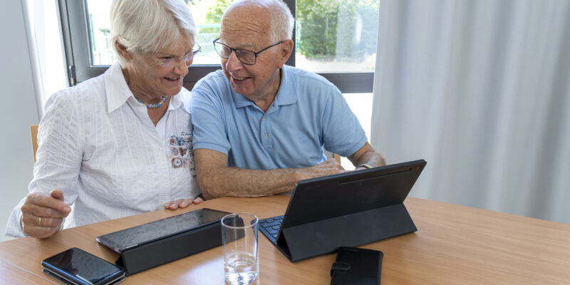 Eine Frau und ein Mann sitzen lächelnd vor einem Tablet.